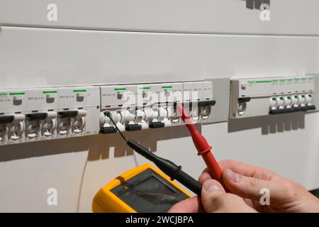 Ein Elektriker, der in einem Schaltschrank arbeitet, prüft Kabel mit einem Tester. Stockfoto