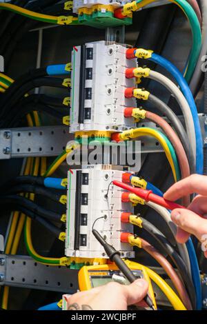 Ein Elektriker, der in einem Schaltschrank arbeitet, prüft Kabel mit einem Tester. Stockfoto