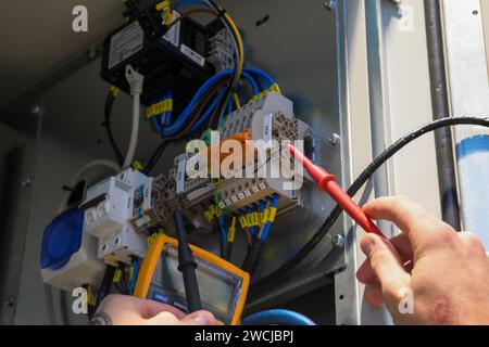 Ein Elektriker, der in einem Schaltschrank arbeitet, prüft Kabel mit einem Tester. Stockfoto