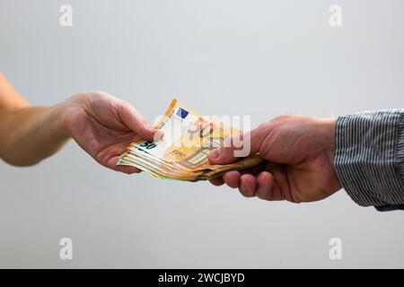 Ein Mann übergibt einer Frau Geld in Form eines Fächers, 50-Euro-Banknoten und 100-Euro-Banknoten, grauer Hintergrund und Nahaufnahme. Stockfoto