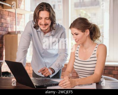 Geschäftsmann und Geschäftsfrau, die sich im Büro treffen. Junge Geschäftsleute diskutieren etwas und zeigen das auf einem Laptop Stockfoto