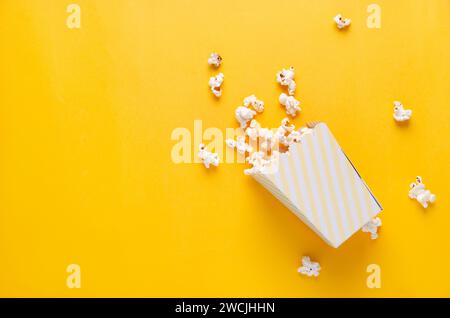 Ein gestreifter Eimer Popcorn auf gelbem Hintergrund, Draufsicht und Kopierraum. Stockfoto