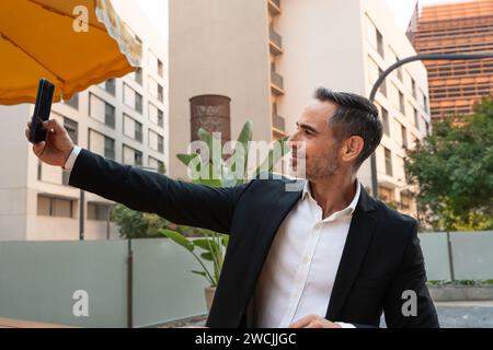 Porträt eines lächelnden Geschäftsmannes, der draußen ein Foto mit einem Smartphone macht. Stockfoto