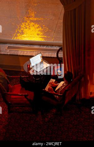 Remote-Mitarbeiter in einem gemütlichen Stuhl mit Laptop bei Regenfällen Stockfoto