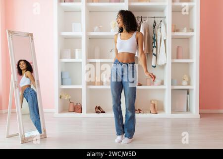 Stilvolle Frau in Jeans, die sich im Spiegel bewundert Stockfoto