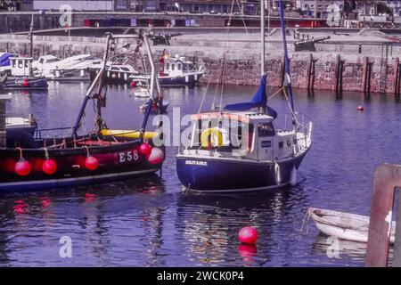 Lyme Regis Harbour, Dorset, 1971. (Auch bekannt als Cobb) kleine Segelboote (Fischerboote) liegen nahe der Hafenmauer. Dieses Bild wurde von der Originalfolie aufgenommen. Rote Steuerbordbojen sind an der Seite eines der Boote zu sehen. Stockfoto