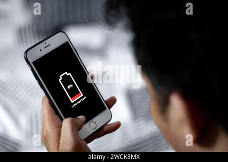 Zelluläre Probleme und Energiekonzepte. Männliche Hand, die ein Smartphone hält, mit dem Symbol für niedrigen Akkustand auf dem Bildschirm. Stockfoto