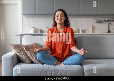 Eine ruhige Frau übt Achtsamkeitsmeditation auf einem gemütlichen Sofa zu Hause Stockfoto