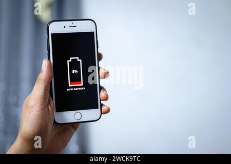 Zelluläre Probleme und Energiekonzepte. Männliche Hand, die ein Smartphone hält, mit dem Symbol für niedrigen Akkustand auf dem Bildschirm. Stockfoto