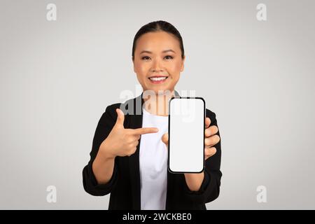 Selbstbewusste asiatische Geschäftsfrau, die ein Smartphone mit einem leeren weißen Bildschirm präsentiert Stockfoto