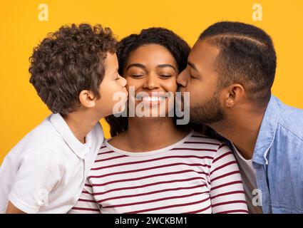 Ein entzückender Sohn und Ehemann, der Küsse auf die Wangen einer lächelnden schwarzen Mutter gibt Stockfoto