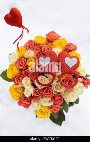 Buntes großes Blumenstrauß aus mehrfarbigen Rosen auf weißem Schneehintergrund. Rotes Souvenir-Herz und herzförmige Brille. Valentinstag. Stockfoto