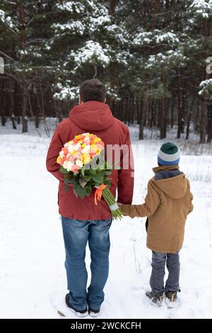 Der Mann hält seinen Sohn in der Hand und versteckt einen großen, bunten Rosenstrauß hinter dem Rücken. Blumen für geliebte Frau und Mutter zum Geburtstag oder Frauentag. A Bitte Stockfoto
