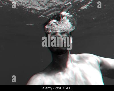 Der Mensch ertrinkt in einem tiefblauen Meer unter dem Wasser mit einem Ausdruck von Schrecken und Angst auf ihrem Gesicht. Schwarzweißfoto mit 3D-Glitcheffekt Stockfoto