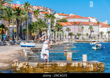 Vorderansicht einer wunderschönen jungen Frau mit Sommerkleid und Hut, die an der Küste in Korcula in Kroatien steht Stockfoto