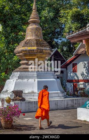 Buddhistischer Mönch, der an einer Tempelstupa im Wat Xieng Thong, Luang Prabang, Laos, vorbeiläuft Stockfoto