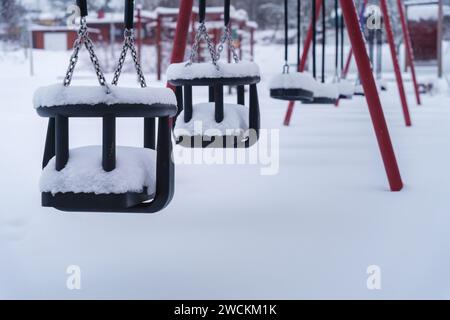 Nahaufnahme der schneebedeckten Schaukeln auf dem leeren Spielplatz im Winter. Finnland. Stockfoto