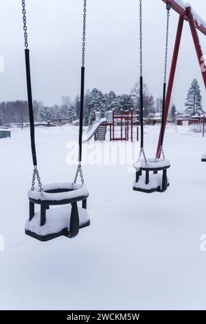 Schneebedeckte Schaukeln auf dem leeren Spielplatz im Winter. Finnland. Stockfoto