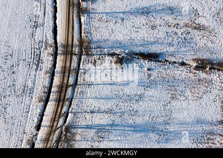 Eine schneebedeckte Straße zwischen Feldern und Wiesen, Blick von einer Drohne. Stockfoto