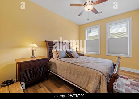 Holzfußboden und -Wände mit weißer Zierleiste in einem Schlafzimmer mit Bettgestell und Deckenventilator Stockfoto