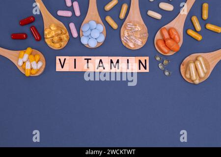 Verschiedene Vitamine in Holzlöffeln mit Text auf grauem Hintergrund. Pillen, Medikamente, Nahrungsergänzungsmittel, Medizin, Apotheke und Gesundheitskonzept. Stockfoto