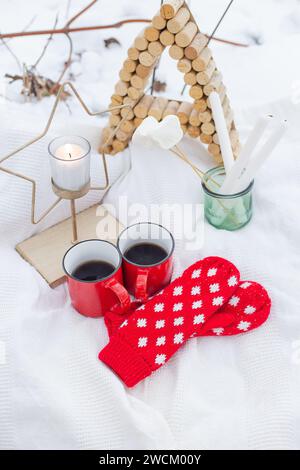 Eine gemütliche Winterszene mit heißen Getränken, Handschuhen und einer Kerze auf einer schneebedeckten Oberfläche. Perfekt für Weihnachtskarten und Wintermotive Stockfoto