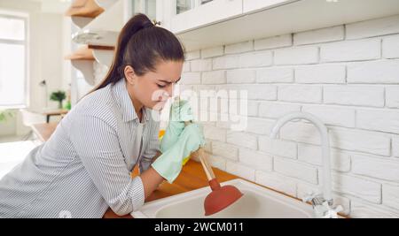 Eine junge Frau, die im Haus arbeitet und versucht, den Clog in der Küchenspüle zu lösen Stockfoto