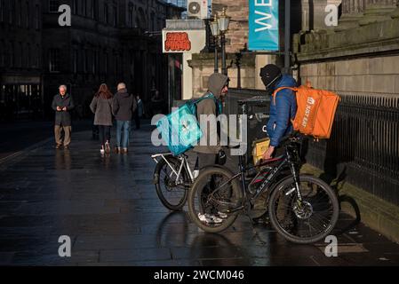 Kuriere zur Lieferung von Fahrradnahrungsmitteln unterhalten sich in der Nicolson Street, Edinburgh, Schottland, Großbritannien. Stockfoto