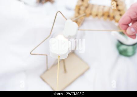 Das Bild zeigt zwei weiße Marshmallows-Spieße auf Schalen, die von einer Person in einem verschneiten Außenbereich gehalten werden Stockfoto