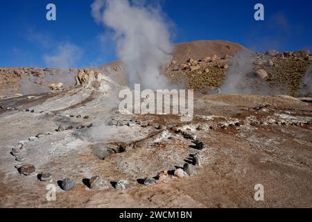 Dampf steigt aus dem Boden, mit Hügeln und blauem Himmel dahinter, in Geysers Del Tatio, Antofagasta, Chile. Stockfoto