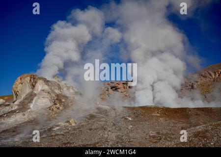 Dampf steigt aus dem Boden, mit Hügeln und blauem Himmel dahinter, in Geysers Del Tatio, Antofagasta, Chile. Stockfoto