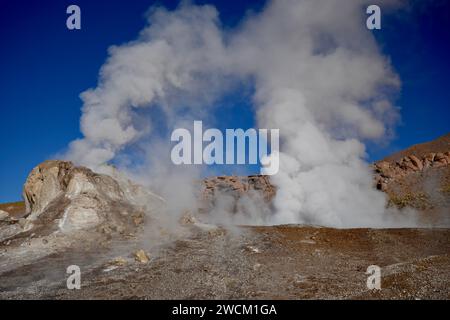 Dampf steigt aus dem Boden, mit Hügeln und blauem Himmel dahinter, in Geysers Del Tatio, Antofagasta, Chile. Stockfoto