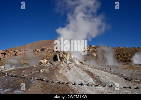 Dampf steigt aus dem Boden, mit Hügeln und blauem Himmel dahinter, in Geysers Del Tatio, Antofagasta, Chile. Stockfoto