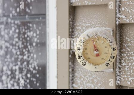 Thermometer mit Schneekappe, das auf einem hölzernen Abstellgleis des Hauses montiert ist und die Temperaturen unter dem Gefrierpunkt anzeigt Stockfoto