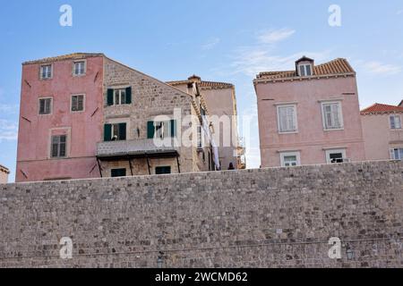 Historische pastellfarbene Gebäude ragen über den befestigten Steinmauern von Dubrovnik, Kroatien, unter einem klaren blauen Himmel. Stockfoto