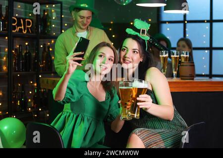 Junge Frauen mit Bier, die Selfie in einem Pub auf der St. nehmen Patrick's Day Stockfoto