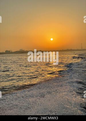 Spektakulärer Sonnenuntergang über dem Meer mit rollenden Wellen, die gegen die Küste krachen Stockfoto
