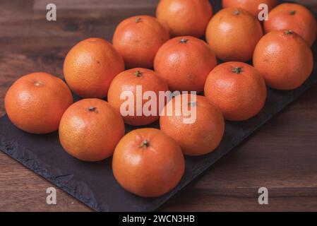 Obst. Foto von Mandarinen in Reihen auf dem schwarzen Steinbrett. Stockfoto