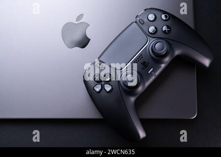 BERLIN, DEUTSCHLAND - 14. JANUAR 2024: Ein Foto eines PS5-Controllers mit zwei Sensen neben einem schlanken Apple MacBook Pro Space Black – perfekt für Spiele Stockfoto