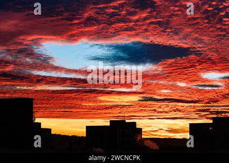 Wunderschöner Sonnenuntergang mit Fallstrichloch im roten feurigen Himmel und einer Silhouette des Gebäudes. Majestätische orangene Wolken mit großer blauer Lücke in der malerischen Winterdämmerung. Stockfoto