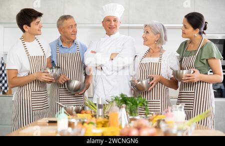 Erfolgreicher männlicher Koch posiert mit der Gruppe beim Kochkurs Stockfoto