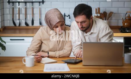 Verheiratete Paare, die in der Küche sitzen und mit Laptop Rechnungen bezahlen, Taschenrechner für die Zählkosten verwenden, Finanzen verwalten, Budgetkontrolle vornehmen, sich gestresst fühlen Stockfoto