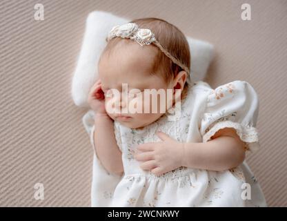 Baby Mädchen Im Kleid Schläft Auf Beigem Stoff Hintergrund Während Der Neugeborenen Foto Sitzung Im Studio Stockfoto