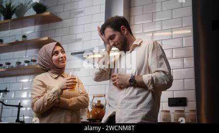 Junges frisch verheiratetes Paar trinkt Orangensaft und hat sich morgens in der Küche unterhalten Stockfoto