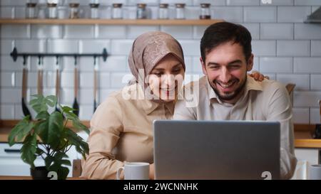 Lächelnde glückliche Paare sprechen Distanz Videoanruf auf Laptop-Webcam in der Küche. Ferngespräche, Live-Videoanrufe mit Familie oder Freunden Konzept Stockfoto