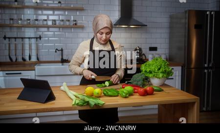 Vlogger junge Chefkochin mit Kopftuch auf der Schürze Aufnahme Video Kochkurs über vegetarische Gerichte oder Salate in der modernen Küche zu Hause. Online b Stockfoto