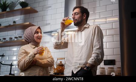 Glückliches Paar trinkt Orangensaft und hat sich morgens im Stehen in der Küche unterhalten Stockfoto