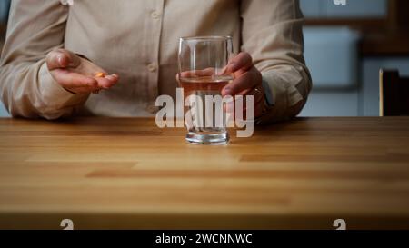 Eine junge Frau nimmt ihre Medizin, während sie in der Küche sitzt Stockfoto