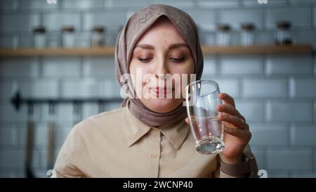 Eine junge Kopftücher-Frau, die ihre Medizin nimmt, während sie in der Küche sitzt Stockfoto