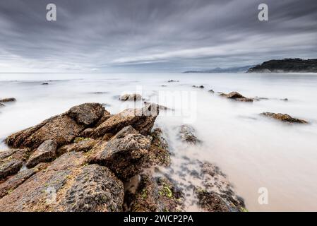 Langzeitbelichtungslandschaft am Strand Lastres bei Sonnenuntergang mit Seideneffekt Meerwasser mit Felsen im Vordergrund, Asturien, Spanien Stockfoto